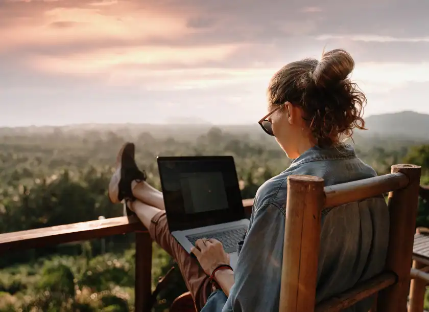 Woman working on a laptop outdoors at sunset, scenic view background.